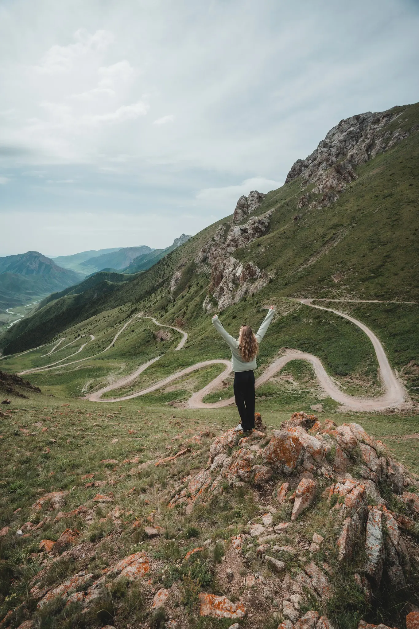 person with arms raised overlooking winding mountain road in Kyrgyzstan