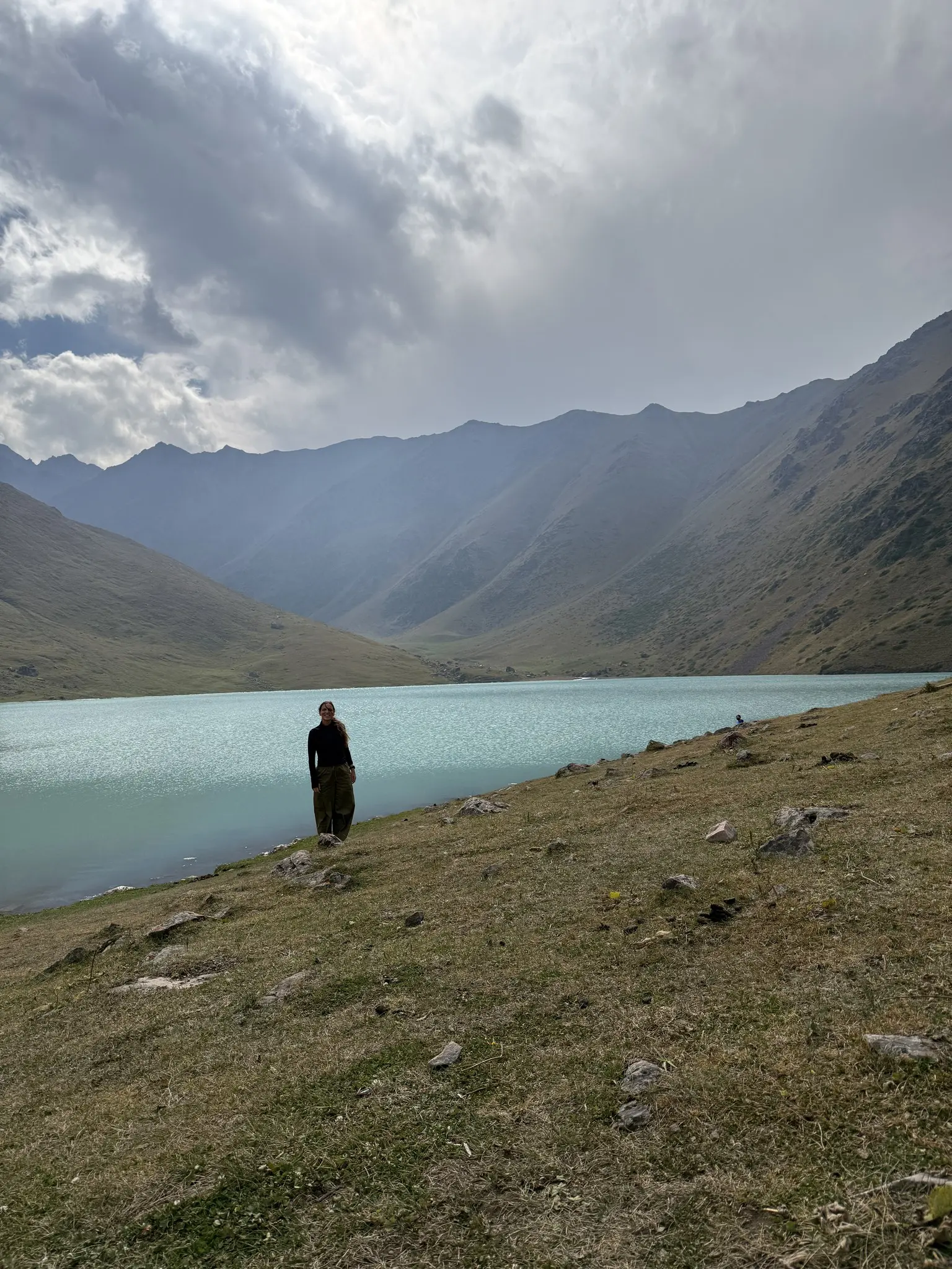 person standing by a turquoise mountain lake in Kyrgyzstan