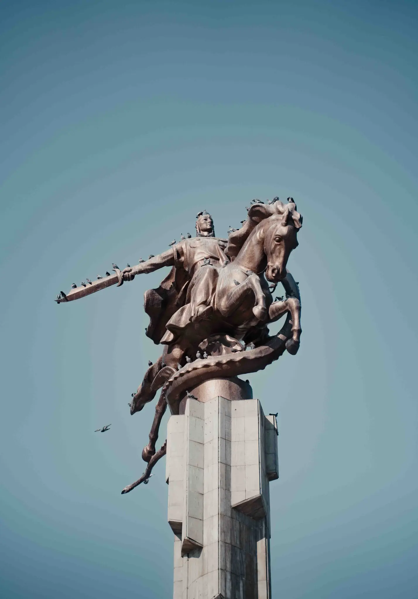 man on horseback statue with birds against blue sky